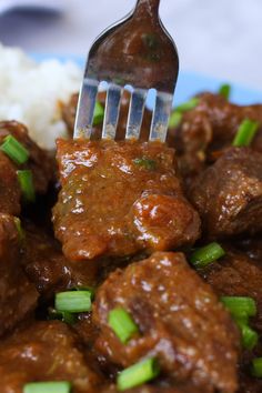 a fork with meat and gravy over rice on a blue plate next to a fork