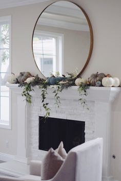 a living room filled with furniture and a fire place covered in greenery next to a round mirror