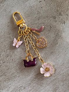 a key chain with charms attached to it on top of a stone surface next to a pink flower