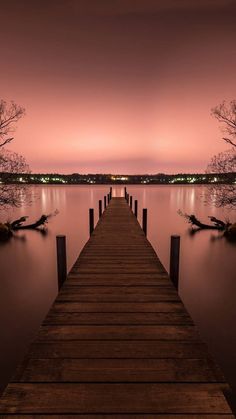 a long wooden dock sitting on top of a lake under a pink sky at night