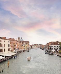 a boat traveling down a river next to tall buildings on both sides and a rainbow in the sky