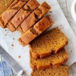 slices of pumpkin bread sitting on top of a white cutting board next to a cup of coffee