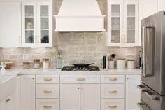 a kitchen with white cabinets and gold pulls on the drawers, an oven and refrigerator