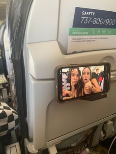 an airplane seat with a cell phone showing two women on the screen and one holding a camera