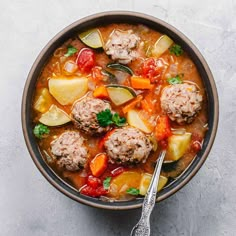 a bowl filled with meatballs and vegetables next to a spoon on a gray surface