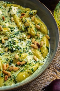 a bowl filled with pasta covered in pesto and pine nuts on top of a table