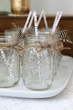 four mason jars with straws tied to them on a white tray next to a gold canister