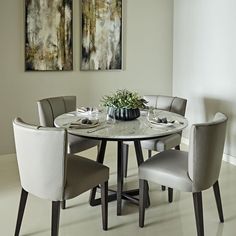 a dining room table with four chairs and a vase on the table in front of two paintings