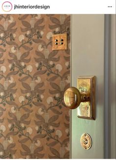 the door handle is brass and has a floral wallpaper behind it, along with two matching knobs