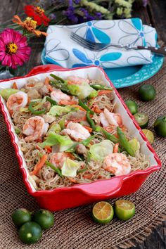 a red dish filled with rice and shrimp next to limes, lemon wedges and flowers