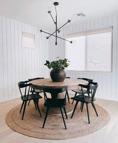 a dining room table with chairs and a vase on the rug in front of it