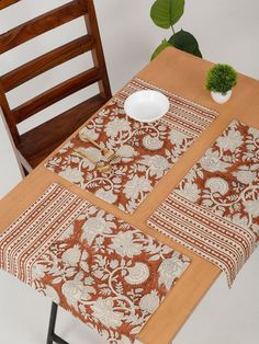 a table with two place mats on it and a wooden chair next to it in front of a potted plant