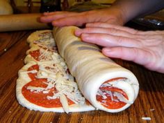 a person holding a long piece of food on top of a wooden table next to a pizza roll