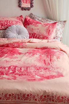 a bed covered in pink and white comforter next to a wall with pictures on it