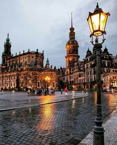 an old town square with people walking around it at night, lit up by street lamps