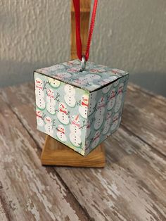 an ornament shaped like a cube with snowmen on it and a red ribbon