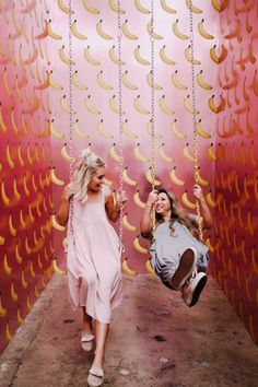 two women in pink dresses swinging on swings with bananas hanging from the ceiling behind them