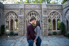 a man and woman kissing in front of an old stone building with arched doorways