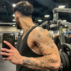 a man with tattoos on his arm holding a barbell in front of a gym machine