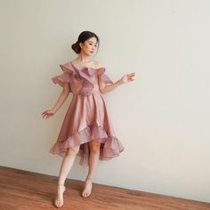 a woman standing in front of a white wall wearing a dress with ruffles