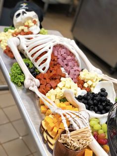 a skeleton made out of food sitting on top of a metal table next to a bowl of fruit