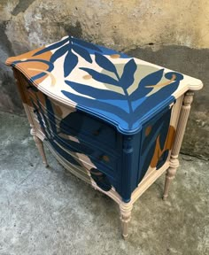 a blue and white painted table sitting in front of a stone wall with leaves on it