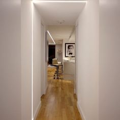 an empty hallway with hard wood flooring and white walls is lit by recessed lighting