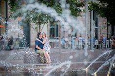 a man and woman sitting on a bench in front of water spouting from the fountain