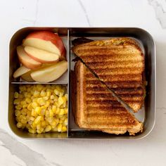 a lunch box with an apple, corn and toast