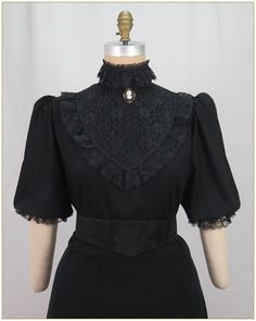 Viscose/Linen. Color: Black. Light weight black linen blend woven fabric blouse with black front lace yoke. Black scalloped edged ruffle lace trim on front bodice, stand up collar and edge of elastic sleeves. Lightly gathered full elbow length sleeves and button back closure. Generously cut for comfort. Dry clean. Circa 1898-1910. Made in U.S.A.  Sizes: SM, MED, LG & XLG. Blouses ordered by bust measurement, inches:  BUST           SIZES 32" - 34"     SMALL 35" - 39"     MEDIUM 40" - 44"     LARGE 45" - 49"     XLARGE Blouses ordered by bust measurement, centimeters: SMALL       81 cm - 86 cm MEDIUM    88.9 cm - 99 cm LARGE      101.6 cm - 111.76 cm XLARGE    114 cm - 124.46 cm HOW TO MEASURE TO DETERMINE YOUR SIZE: BUST: Measure the fullest part of your bust, we add the fitting ease and s Elegant Black Tops With Contrast Lace, Gothic Black Top With Lace Collar, Black Gothic Blouse For Formal Occasions, Black Fitted Blouse With Ruffled Collar, Formal Black Tops With Lace Cuffs, Black Lace Patchwork Short Sleeve Blouse, Black Short Sleeve Blouse With Lace Patchwork, Black Fitted Top With Peter Pan Collar, Elegant Black Blouse With Lace Cuffs