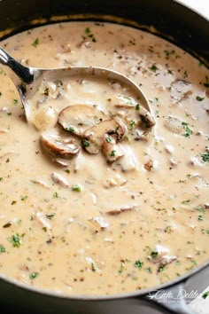 a pot filled with mushroom soup on top of a wooden table next to a spoon