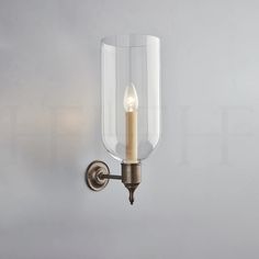 a wall mounted light with a candle on it's side and a clear glass shade