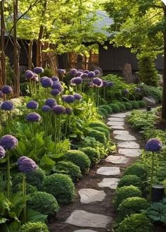 a garden filled with lots of purple flowers and green plants next to a stone path