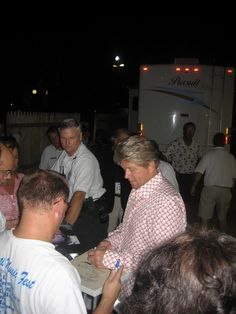 a group of people standing around a table in front of a white truck at night