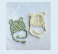 two crocheted hats are laying next to each other on a white sheet,