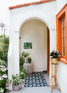 a white house with an orange door and potted plants on the side walk way