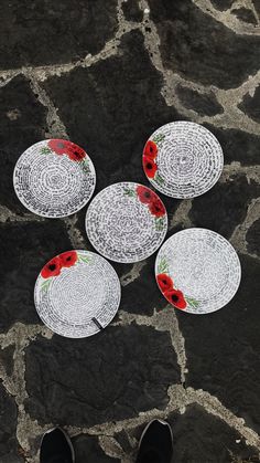 four white plates with red flowers on them sitting on a stone floor next to a pair of black shoes