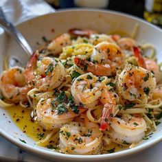 a white bowl filled with pasta and shrimp on top of a table next to a fork