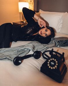 a woman laying on top of a bed next to an old fashioned telephone and blanket