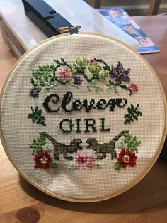 there is a cross - stitch pattern on the hoop with flowers and words that read, clever girl