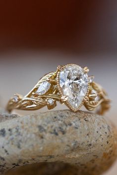 a gold ring with a pear shaped diamond in it on top of a stone surface