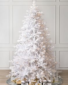 a white christmas tree with presents under it on a tray in front of a wall