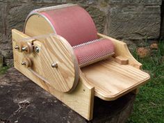 a wooden spinning machine sitting on top of a tree stump in front of a stone wall