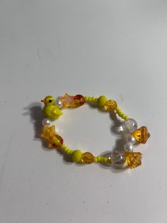 a yellow bracelet with beads and charms on white table top next to small plastic fish