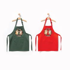 two children's aprons hanging on wooden hangers, one green and the other red