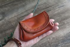 a hand holding a brown leather wallet on top of a wooden table