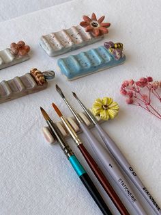 several different types of art supplies on a white tablecloth with flowers and other items