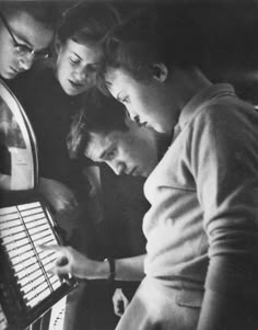 black and white photograph of four people looking at an electronic device