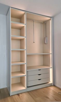 an empty white closet with drawers and lights on the shelves, in front of a door