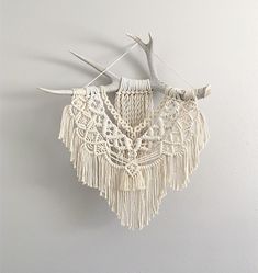 a white wall hanging with antlers and crocheted fringes on it's sides